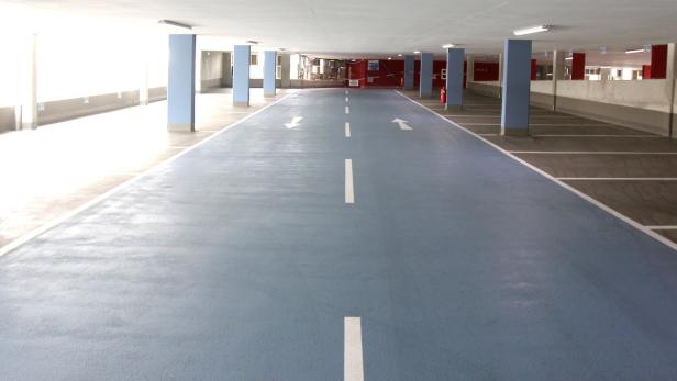 Eine leere, hell erleuchtete Tiefgarage mit blauen Säulen und Fahrbahnmarkierungen.