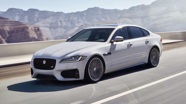 Ein weißer Jaguar XF fährt auf einer Straße vor einer Bergkulisse.