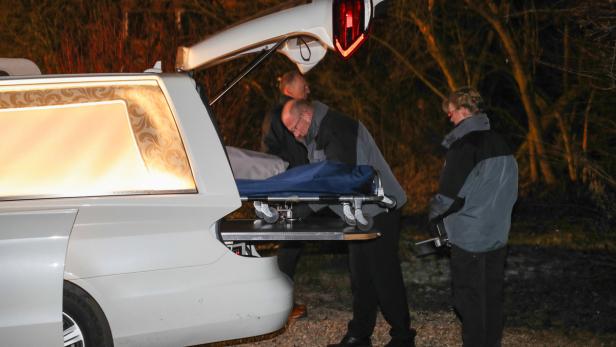 Zwei Männer schieben einen Sarg aus einem Leichenwagen.