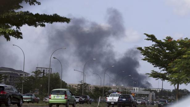 Dichter, dunkler Rauch steigt über einer belebten Straße mit Autos auf.