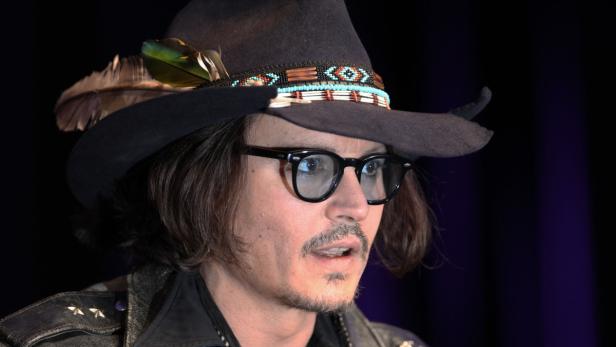 Johnny Depp mit Hut, Brille und Bart vor dunklem Hintergrund.