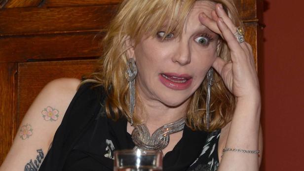 Courtney Love mit Schmuck und Tattoos blickt überrascht.