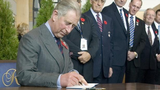König Charles III. unterzeichnet ein Dokument in Anwesenheit anderer Personen.