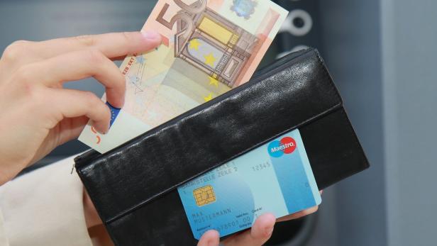 Eine Person steckt einen 50-Euro-Schein in eine schwarze Geldbörse mit einer Maestro-Karte.