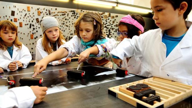 Eine Gruppe Kinder arbeitet mit Farbwalzen an einer Druckplatte.