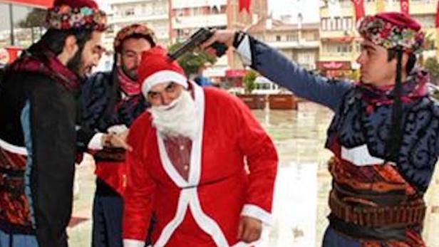 Männer in Tracht bedrohen einen als Weihnachtsmann verkleideten Mann mit einer Pistole.