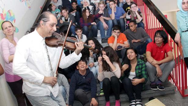 Ein Geiger spielt vor einer Gruppe von Schülern auf einer Treppe.