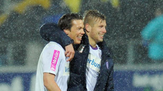 Zwei lächelnde Fußballspieler umarmen sich im Regen.