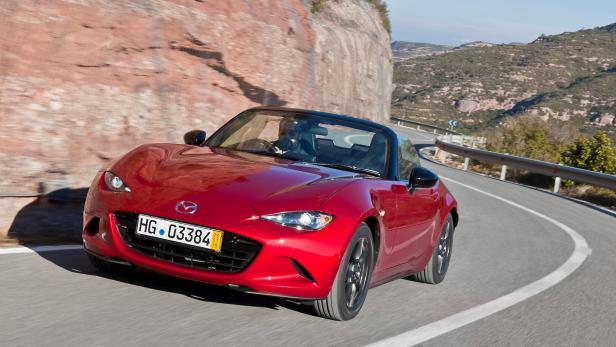 Ein roter Mazda MX-5 fährt auf einer kurvenreichen Straße entlang einer Felswand.