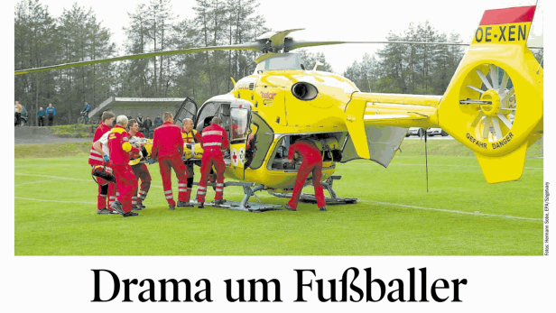 Ein gelber Rettungshubschrauber steht auf einem Fußballfeld, Sanitäter eilen zu Verletzten.