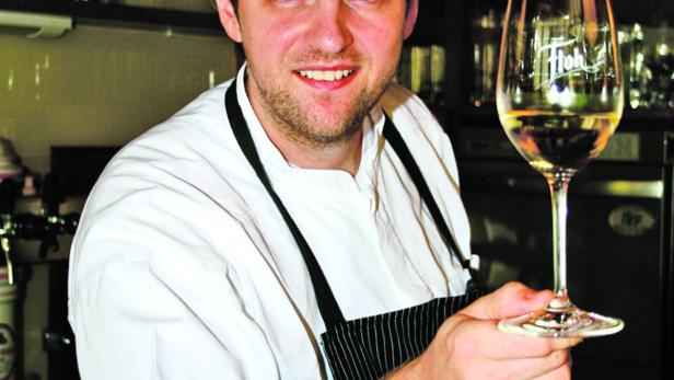 Ein lächelnder Koch präsentiert ein Glas Weißwein.