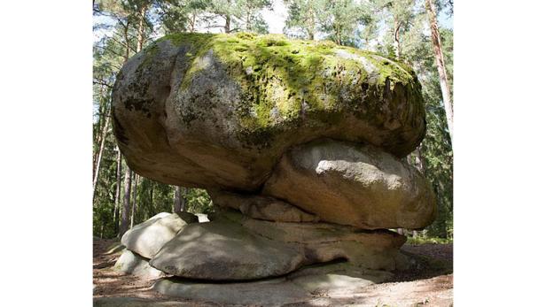 Ein großer, moosbedeckter Felsen balanciert auf kleineren Steinen in einem Wald.