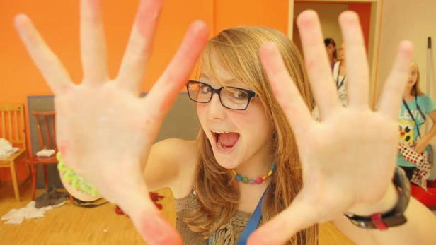 Ein junges Mädchen mit Brille zeigt ihre bemalten Hände in die Kamera.