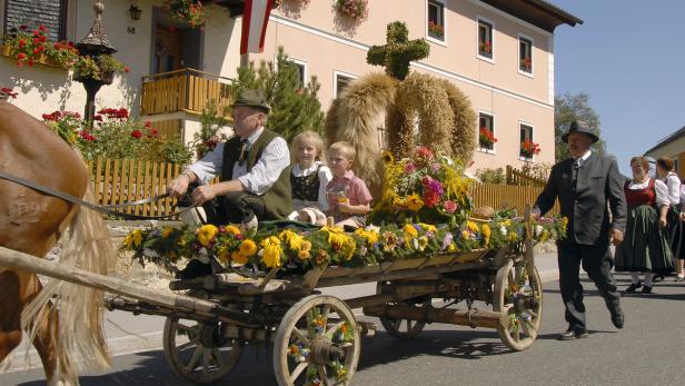 Ein festlich geschmückter Pferdewagen mit Menschen in Tracht fährt durch ein Dorf.
