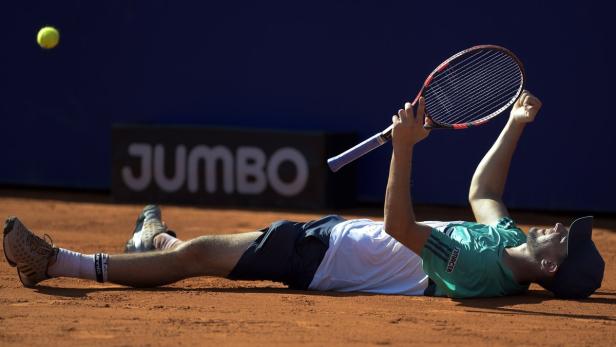 Ein Tennisspieler liegt erschöpft mit seinem Schläger auf dem Sandplatz.