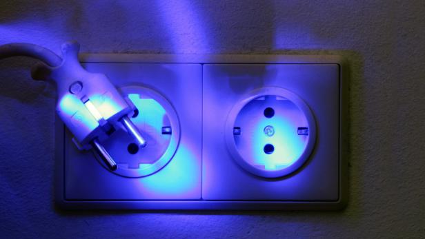 Ein Stecker steckt in einer Steckdose, beide sind bläulich beleuchtet.