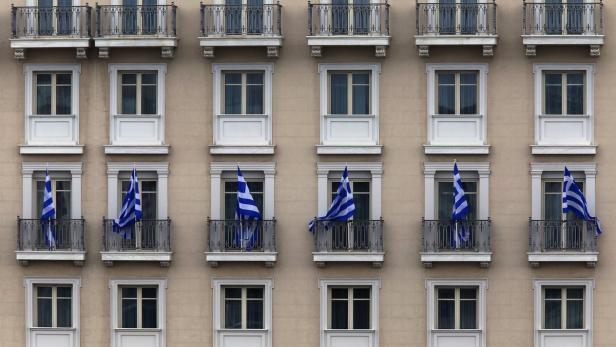 Die Fassade eines Gebäudes ist mit griechischen Flaggen an den Balkonen geschmückt.