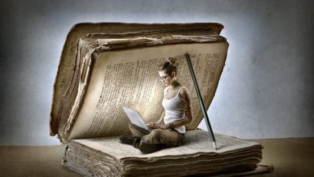 Eine junge Frau mit Tätowierungen sitzt auf einem riesigen Buch und benutzt einen Laptop.