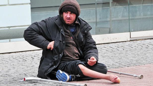 Ein obdachloser Mann sitzt mit Krücken auf dem Boden.