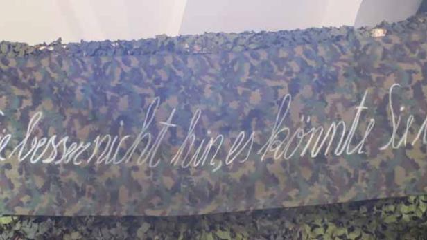 Ein Banner mit Tarnmuster und der Aufschrift: „Schauen Sie besser nicht hin, es könnte Sie berühren!“.