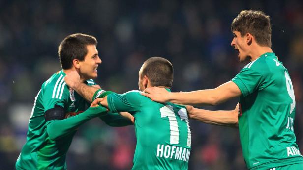 Drei Fußballspieler in grünen Trikots feiern gemeinsam ein Tor.