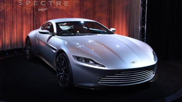 Ein silberner Aston Martin, der im Hintergrund vor einem „Spectre 007“-Banner steht.