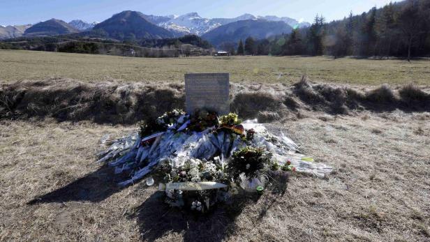 Ein Denkmal mit Blumen und Kränzen auf einem Feld vor einer Bergkulisse.