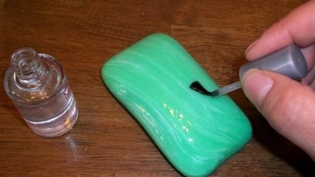 Eine Hand bemalt ein grünes Stück Seife mit schwarzem Nagellack.