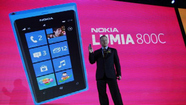 Ein Mann präsentiert das Nokia Lumia 800C Smartphone vor einem pinkfarbenen Bildschirm.