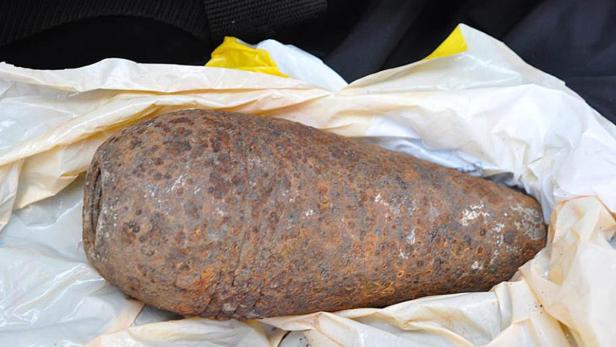 Eine rostige, birnenförmige Bombe liegt in einer Plastiktüte.