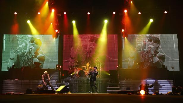 Eine Band tritt auf einer Bühne mit großen Bildschirmen und bunten Lichtern auf.