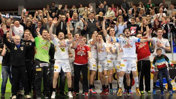 Eine jubelnde Handballmannschaft feiert mit einem Pokal vor ihren Fans.