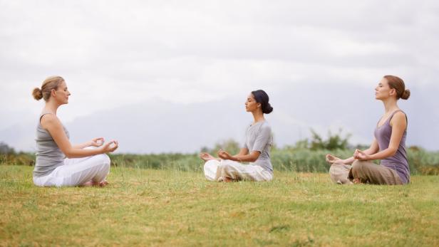 Drei Frauen sitzen im Freien und praktizieren Yoga.