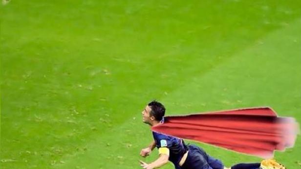 Ein Fußballspieler mit einem roten Umhang springt auf einem grünen Feld.