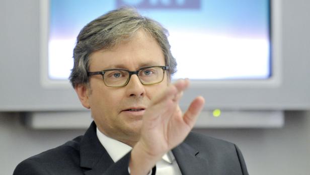 Ein Mann mit Brille gestikuliert vor einem Bildschirm.