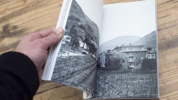 Eine Hand blättert in einem Buch mit Schwarzweißfotografien von Weinbergen und Häusern.