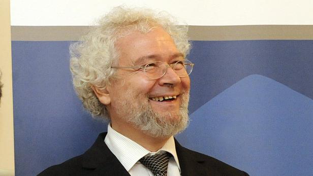 Ein lächelnder Mann mit Bart und Brille vor einem blauen Hintergrund.