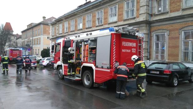 Feuerwehrleute stehen neben einem roten Feuerwehrauto mit der Aufschrift „Feuerwehr Notruf 122“.