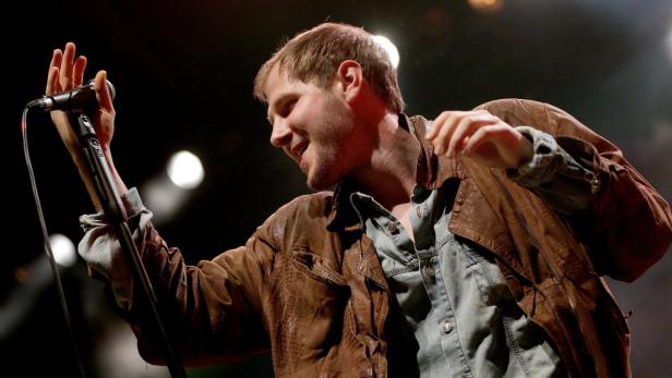 Ein Mann mit brauner Jacke singt in ein Mikrofon.