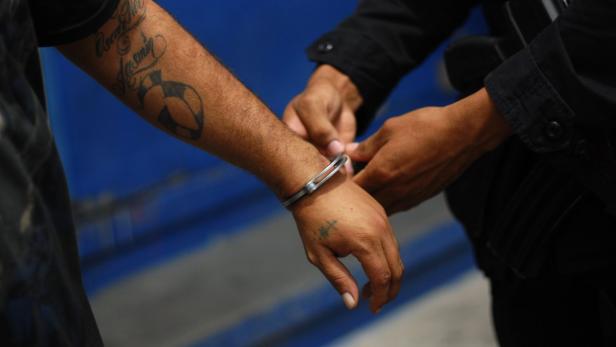 A policeman places handcuffs on a MS13 gang member