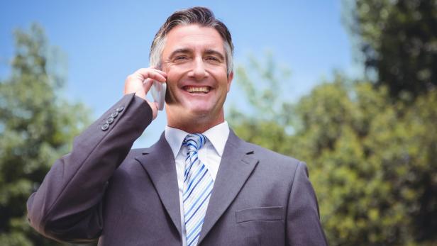Ein lächelnder Mann im Anzug telefoniert im Freien.