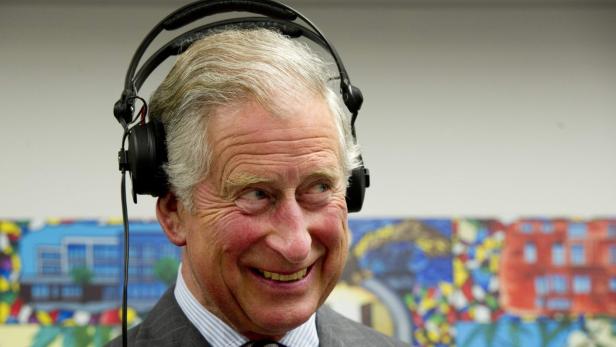 König Charles III. lächelt mit Kopfhörern auf dem Kopf.