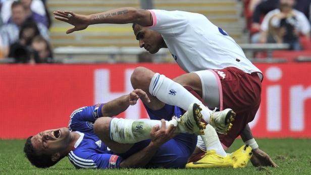 Ein Fußballspieler liegt verletzt am Boden, während ein anderer über ihn gebeugt steht.