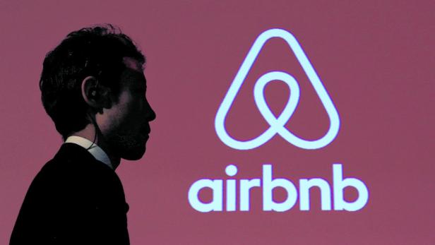 Ein Mann im Anzug steht vor dem Airbnb-Logo.
