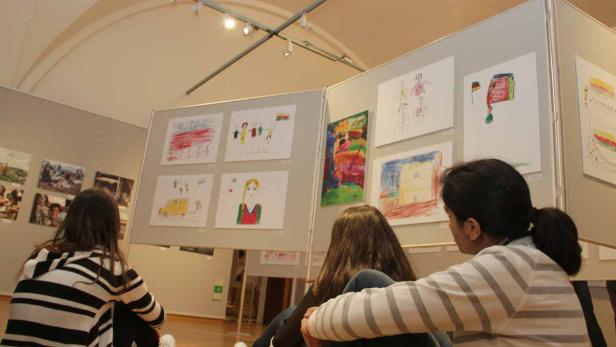 Zwei Mädchen betrachten eine Ausstellung mit Kinderzeichnungen.