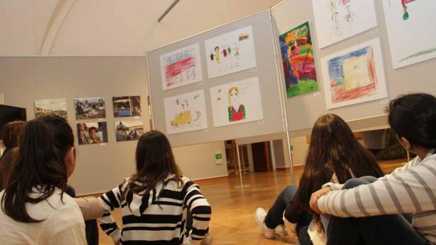 Kinder betrachten eine Ausstellung mit Kinderzeichnungen.