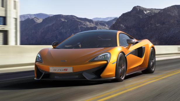 Ein orangefarbener McLaren 570S fährt auf einer Straße vor einer Bergkulisse.