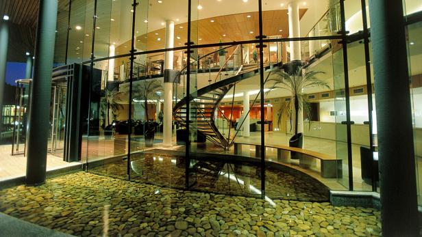 Die Lobby eines Hotels mit Wendeltreppe, Wasserbecken und tropischen Pflanzen.