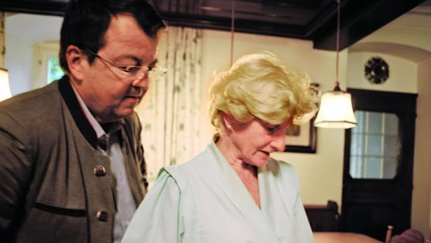 Ein Mann in Trachtenjacke und eine ältere Frau in einem Innenraum.