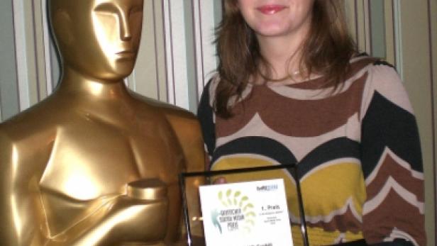 Eine Frau hält eine Auszeichnung neben einer goldenen Oscar-Statue.